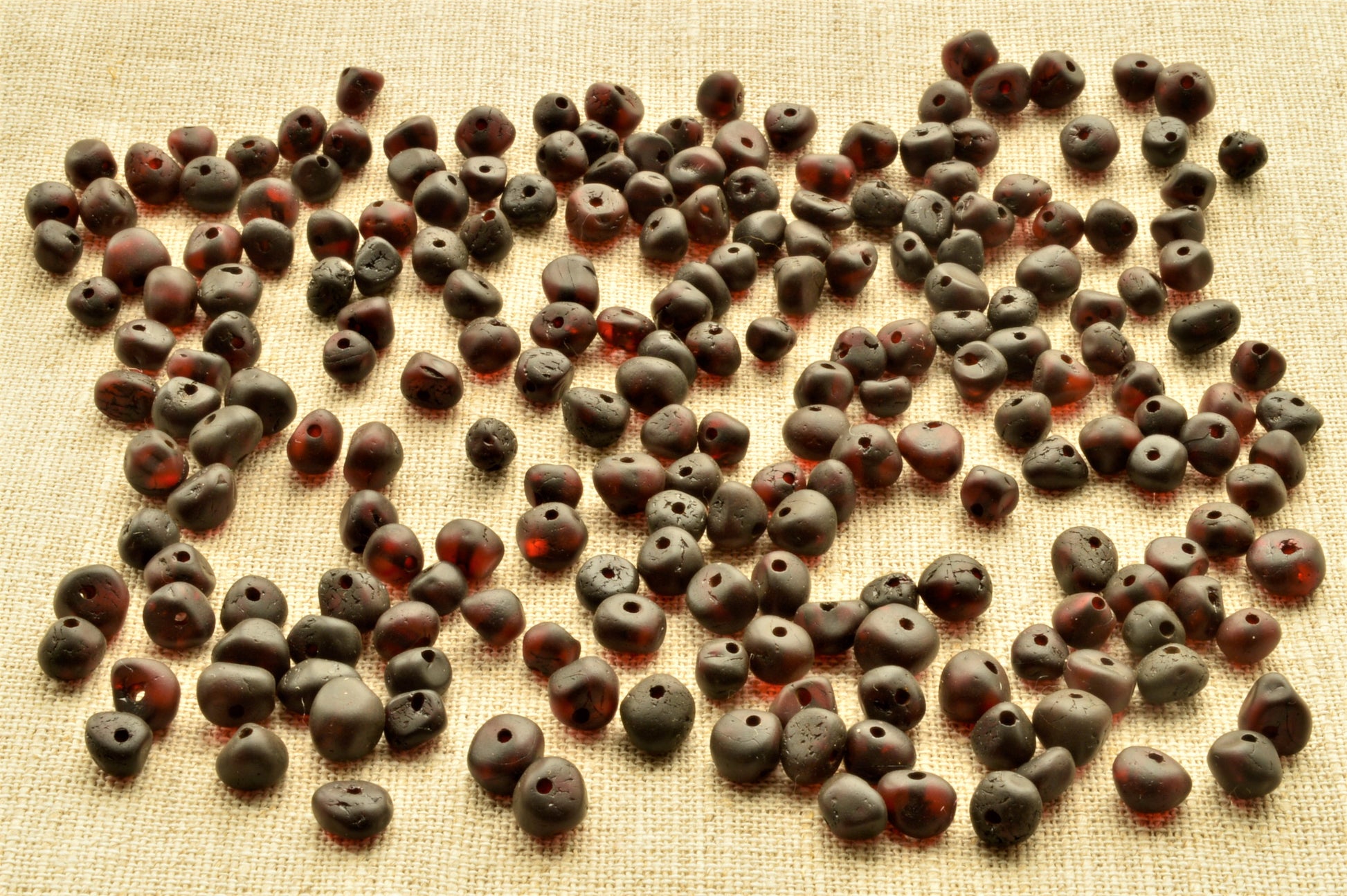 Dark brown clay beads scattered on a textured beige surface