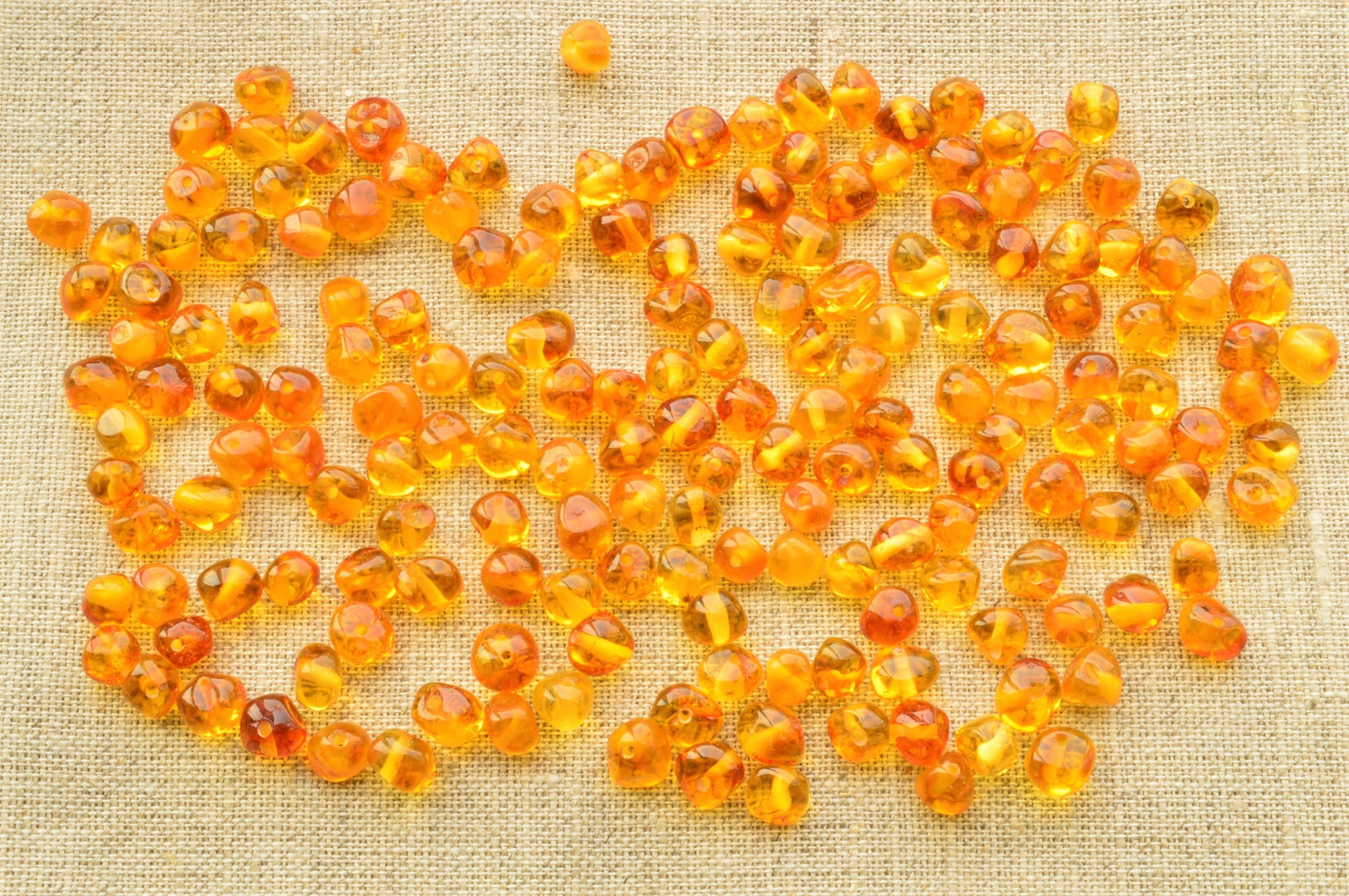 Orange beads scattered on a textured beige fabric background