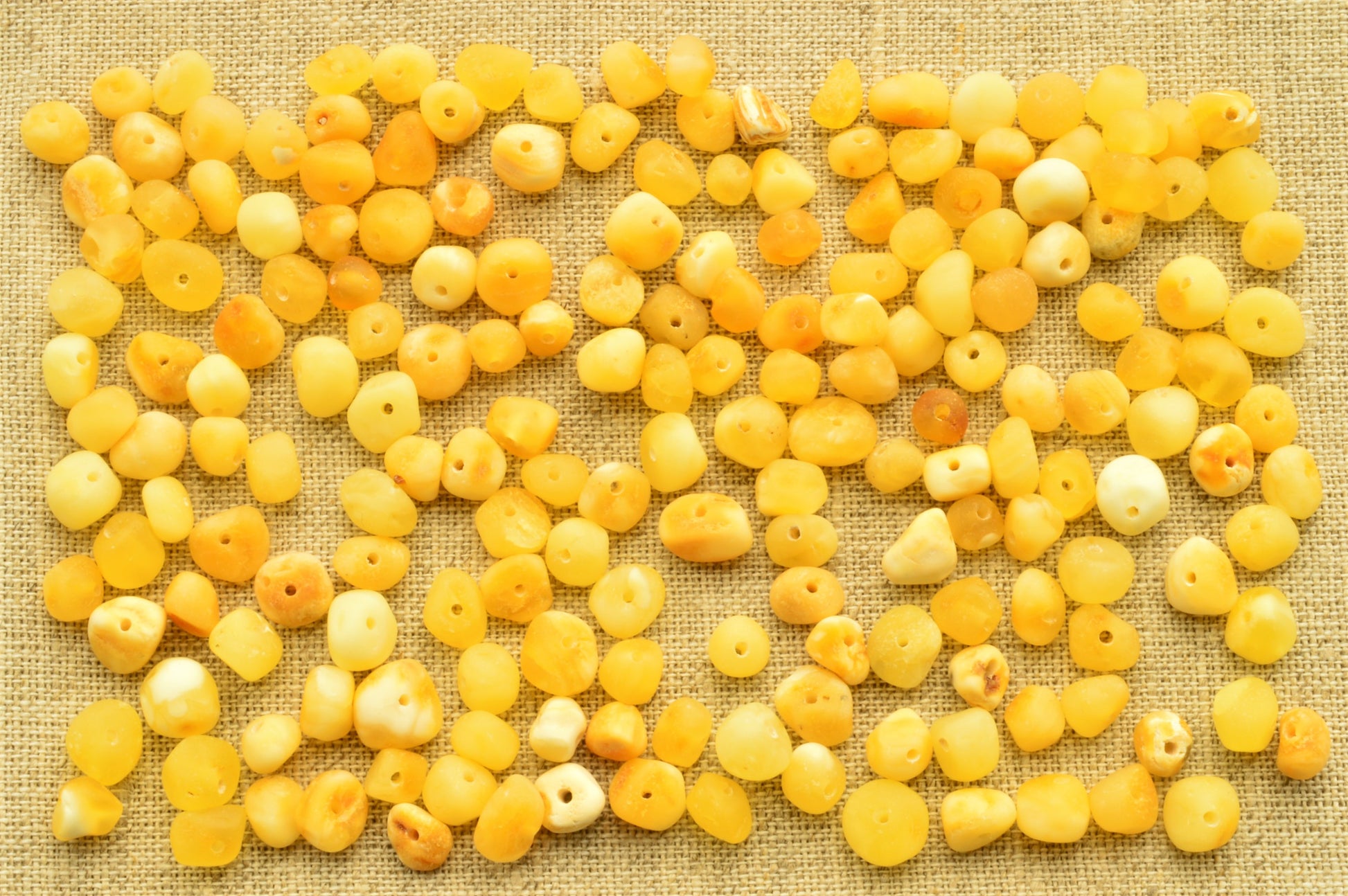 Yellow beads scattered on a textured beige fabric background