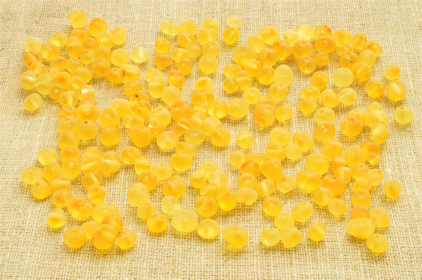 Yellow beads scattered on a textured beige fabric background