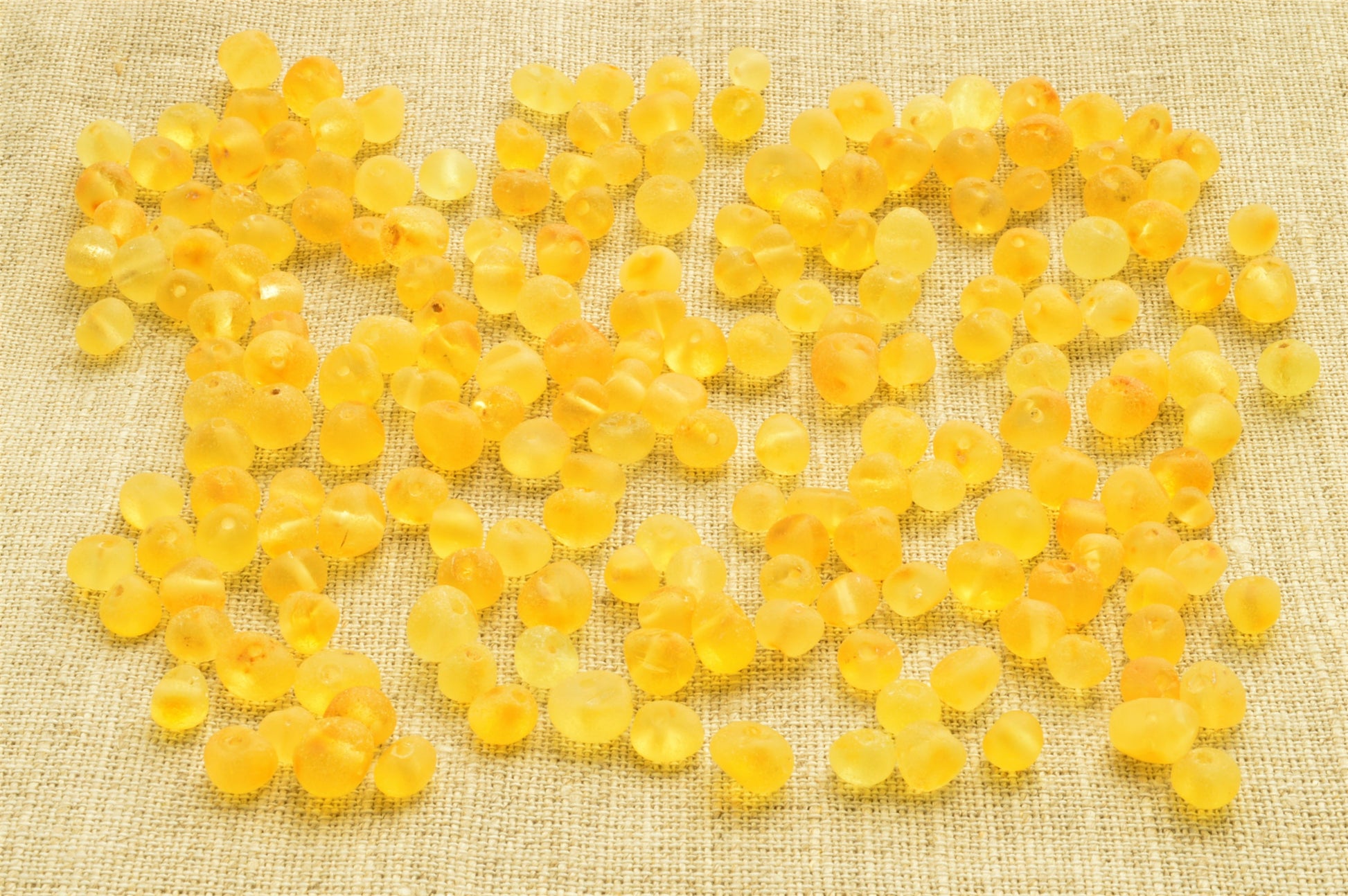 Yellow beads scattered on a textured beige fabric background