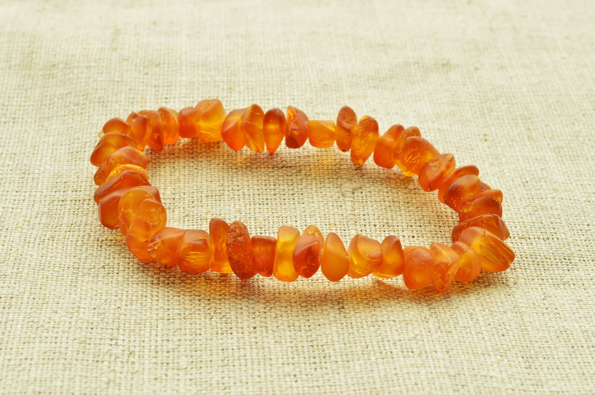 Orange beaded bracelet on a textured beige fabric background