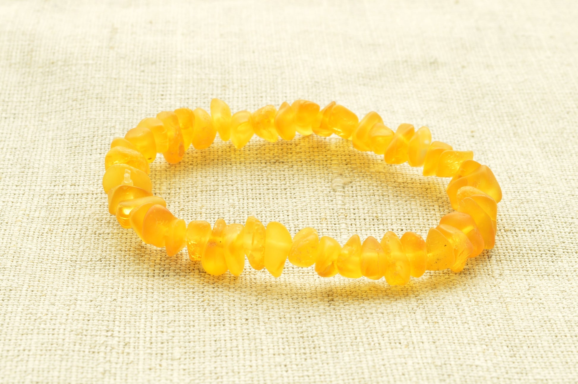 Yellow beaded natural baltic amber bracelet on a textured beige fabric background