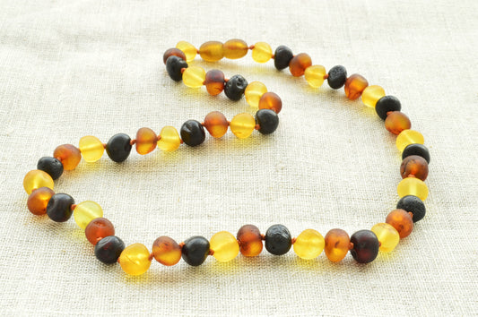 Multicolored beaded necklace on a textured fabric background natural baltic amber knotted raw baroque neckace