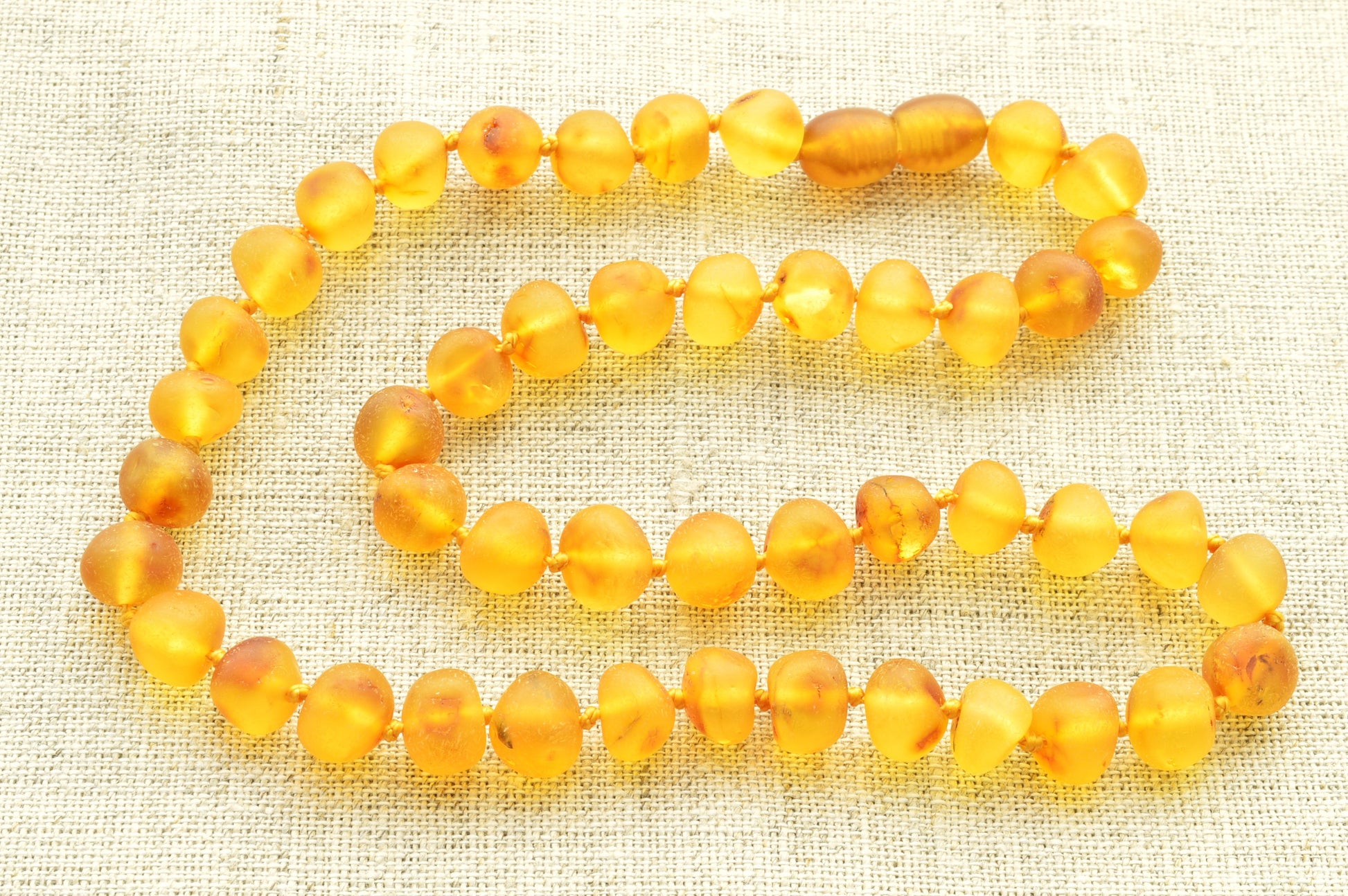 Beaded amber necklace on a textured beige fabric background natural baltic amber knotted raw baroque neckace