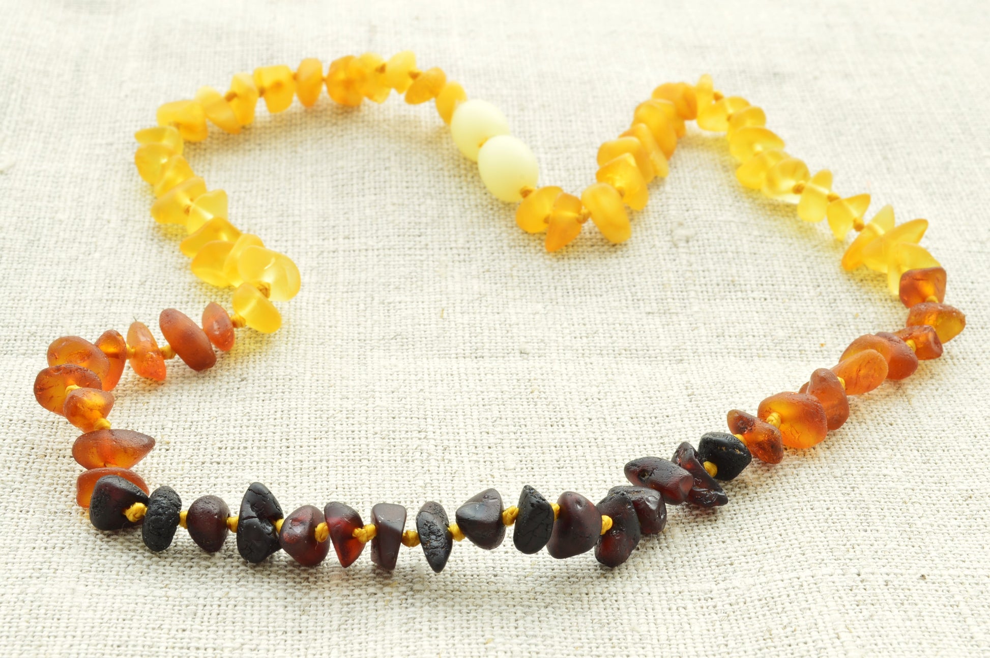 Necklace with multicolored beads forming a heart shape on a light fabric background