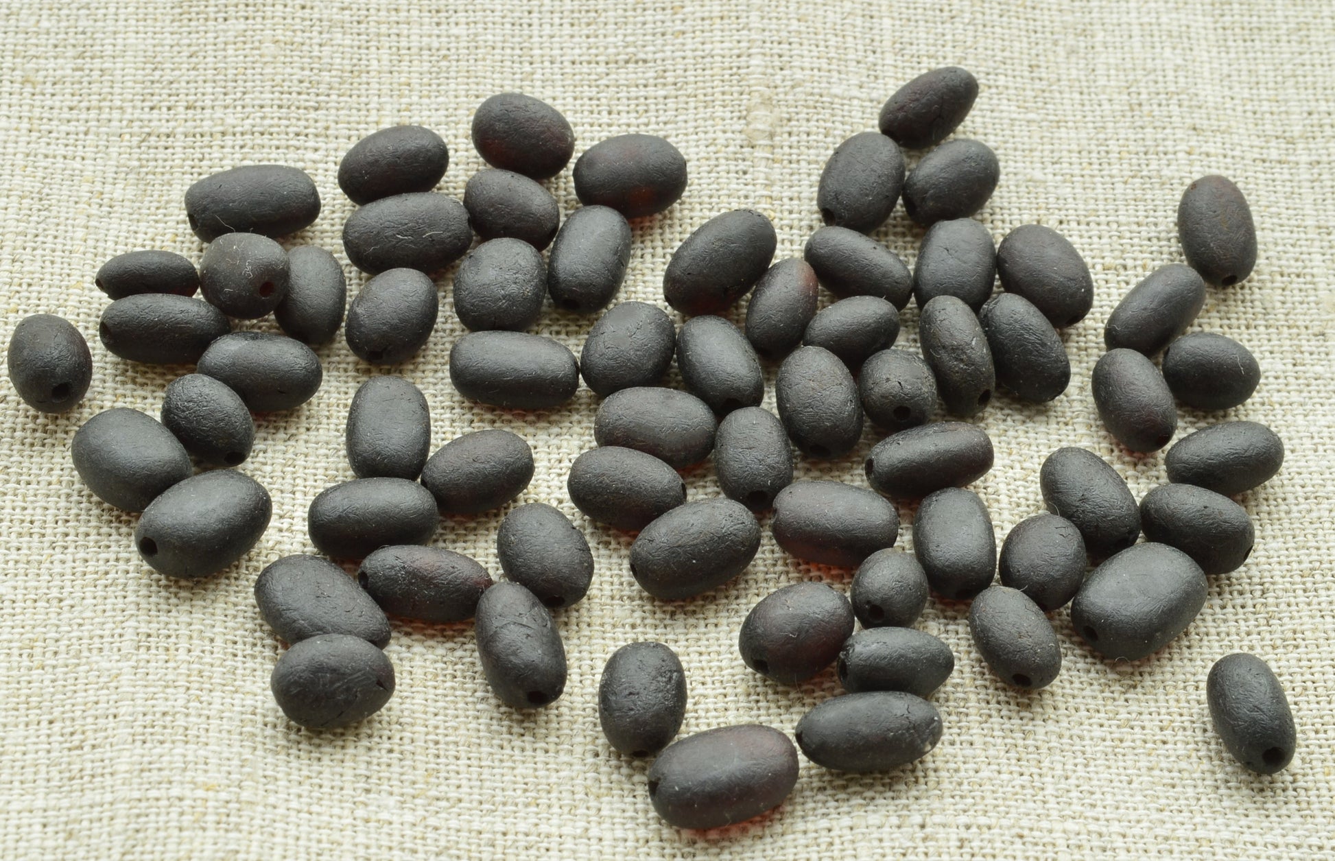 natural baltic amber loose beads oblong raw unpolished on a textured beige surface