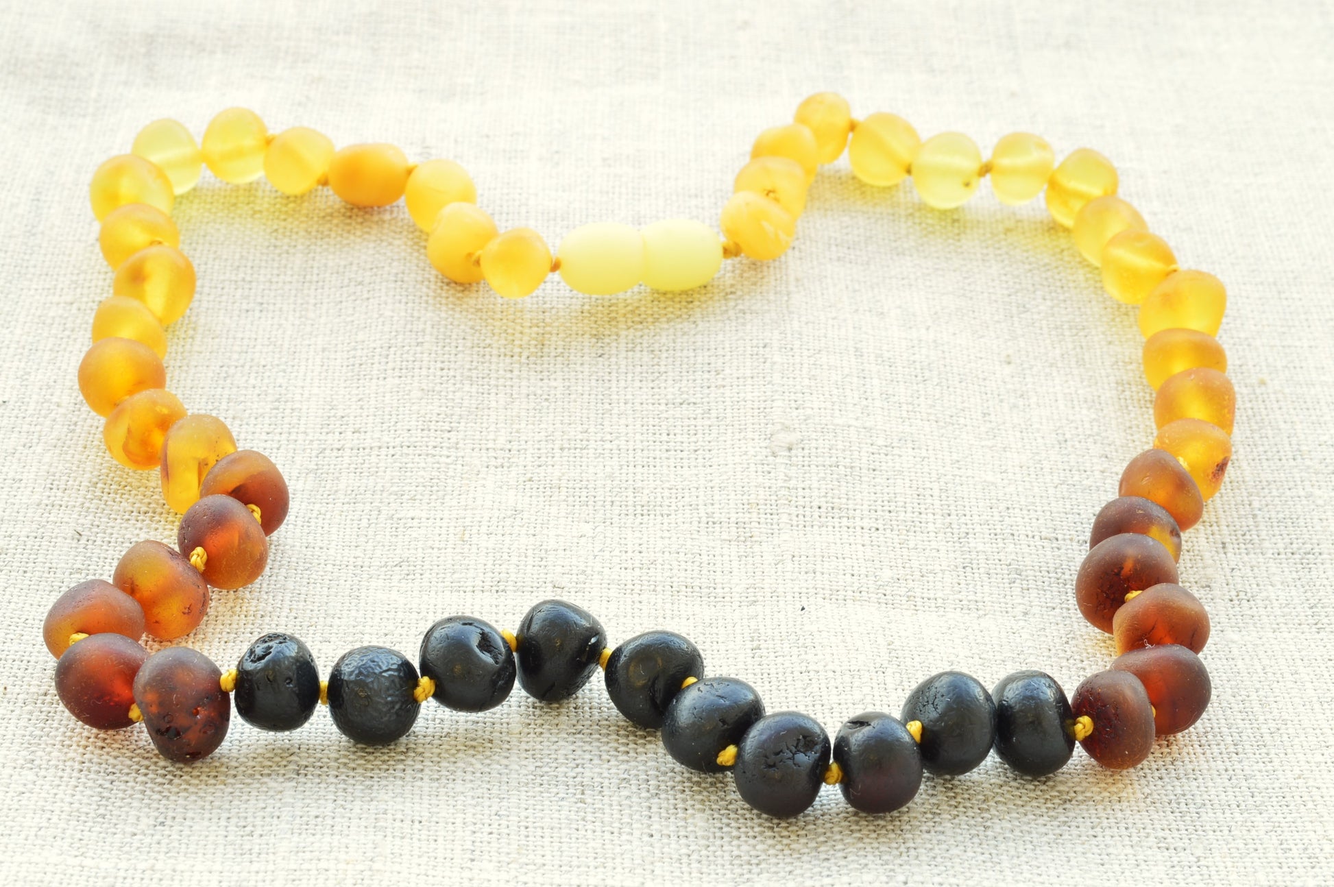 Multicolored beaded necklace forming a heart shape on a textured fabric background