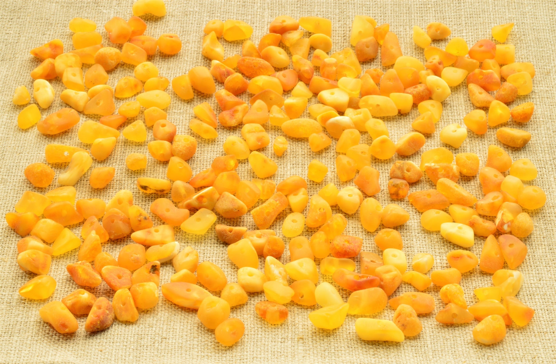 Yellow and natural baltic amber raw unpolished chip beads on a textured beige background