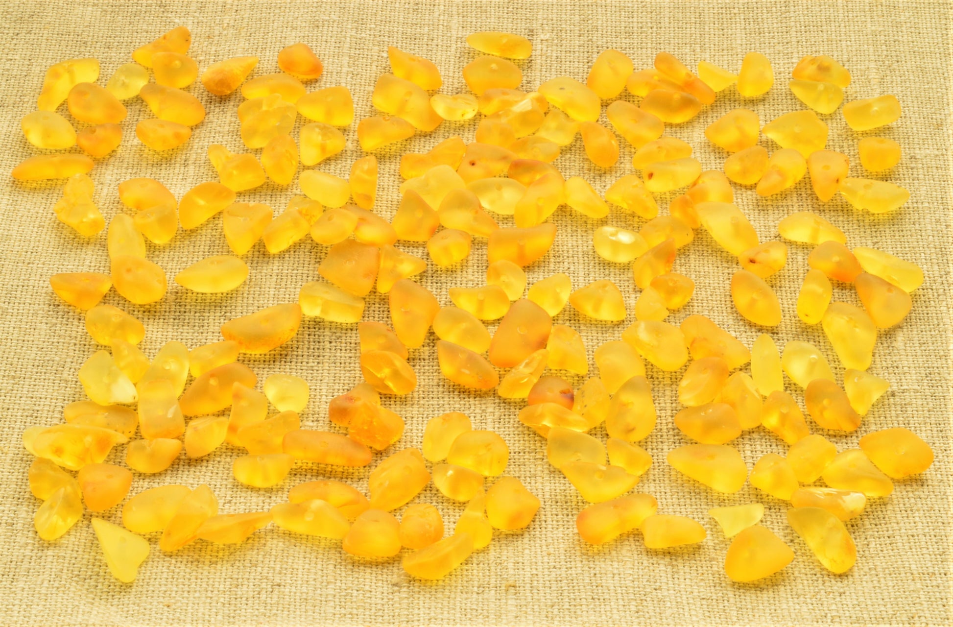 Yellow natural baltic amber raw unpolished chip beads chips on a textured beige fabric background
